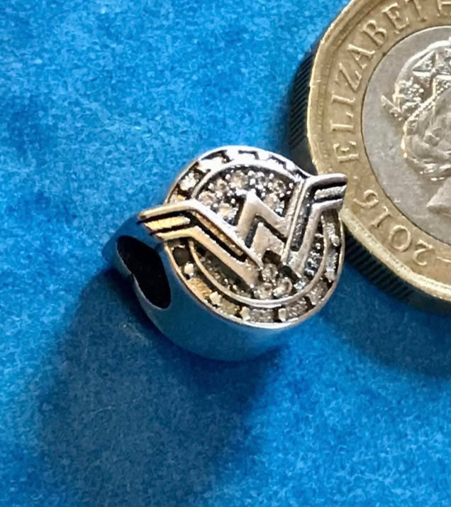 Silver Wonder Woman charm next to a British coin on a blue background