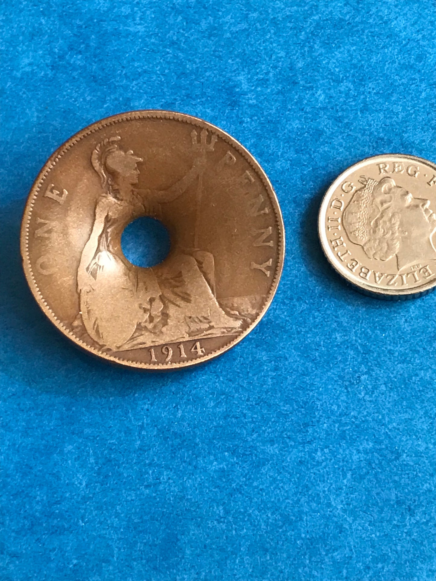 World War One Dated 1914 Coin damaged by Shrapnel on a blue background next to a British coin for scale