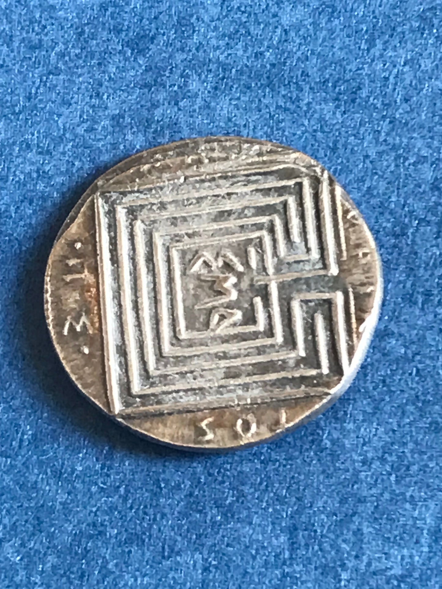 Silver coin with geometric design on a blue background
