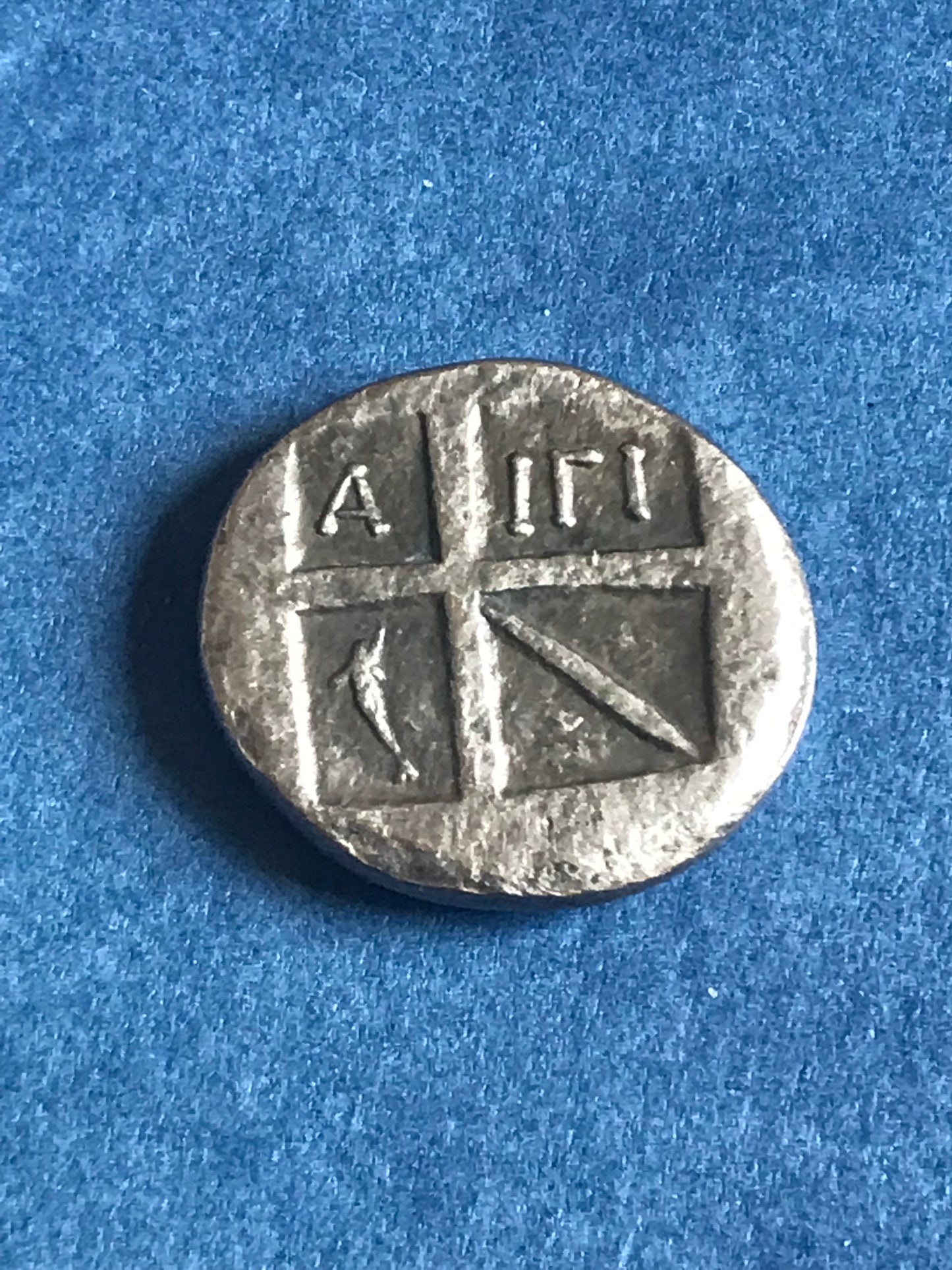 Silver coin with Greek symbols on a blue background