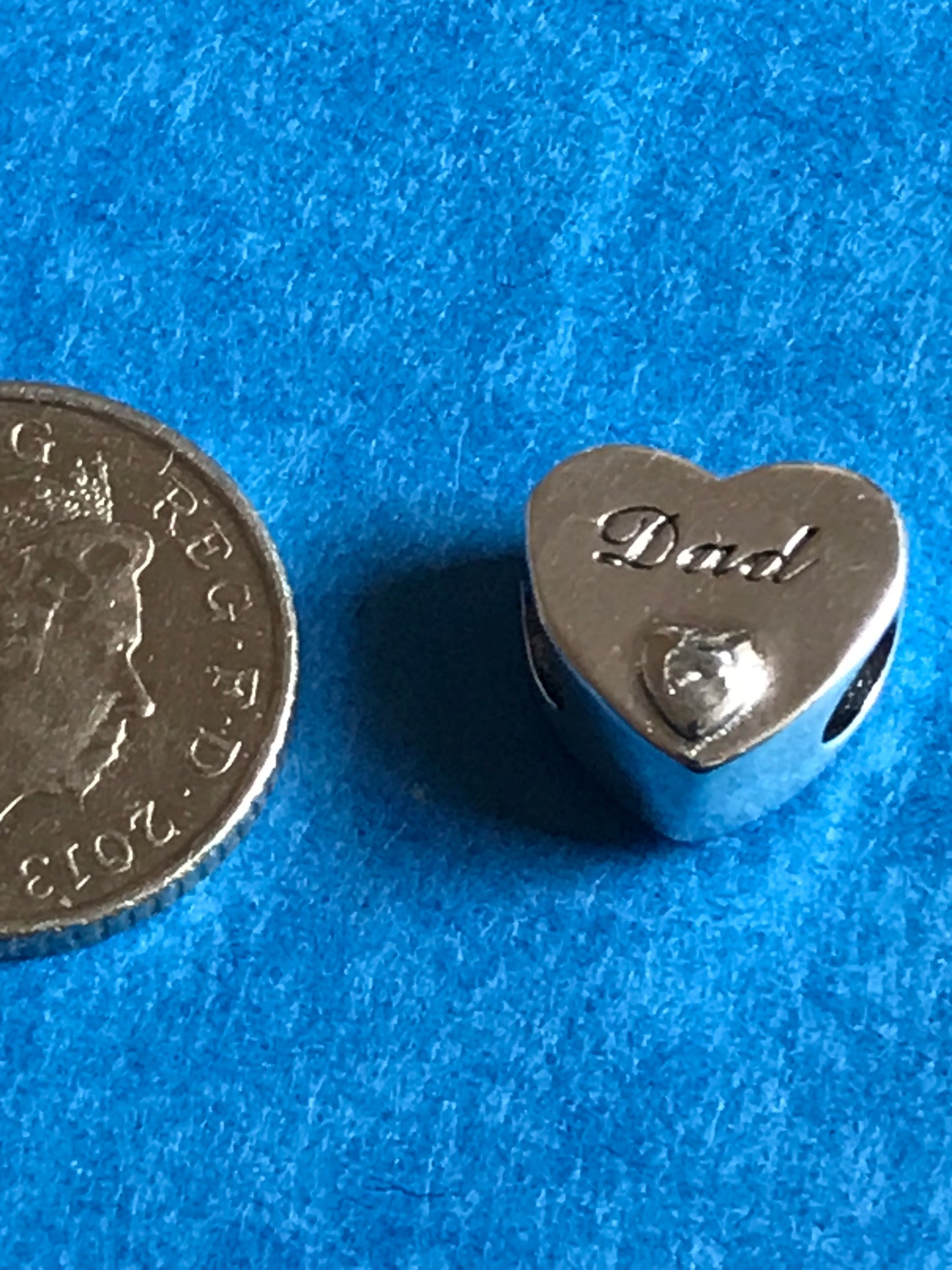Heart-shaped Silver Dad charm with 'dad' engraving on a blue background for charm bracelet