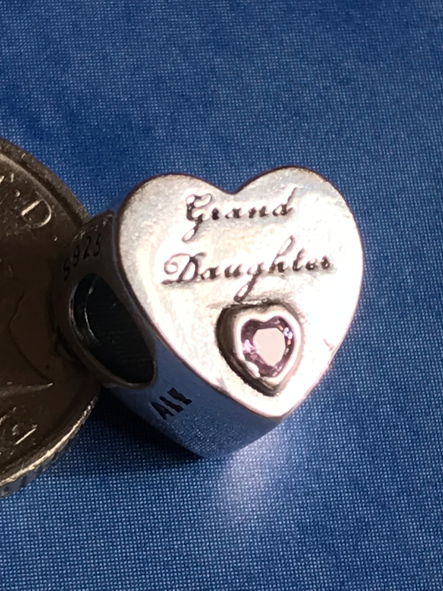 Heart-shaped silver charm with engraved text on a blue fabric background
