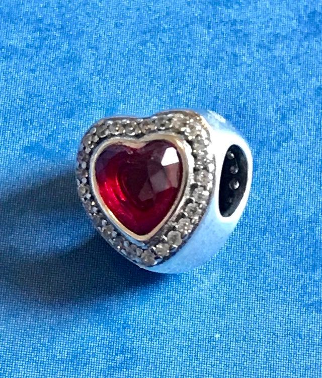 Heart-shaped charm with red center and silver border on a blue fabric background