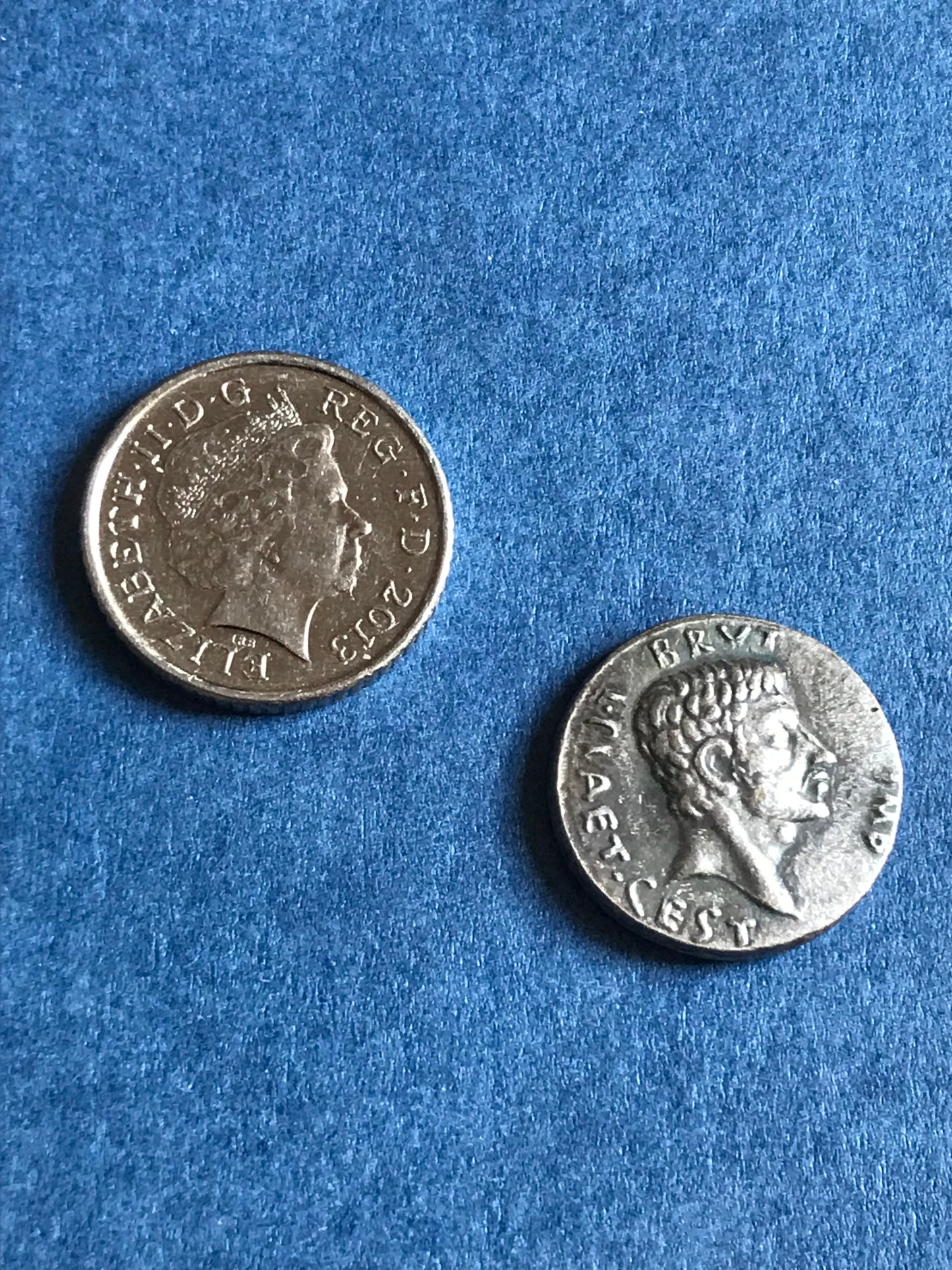 Ancient Roman coin next to a British coin for scale on a blue textured background