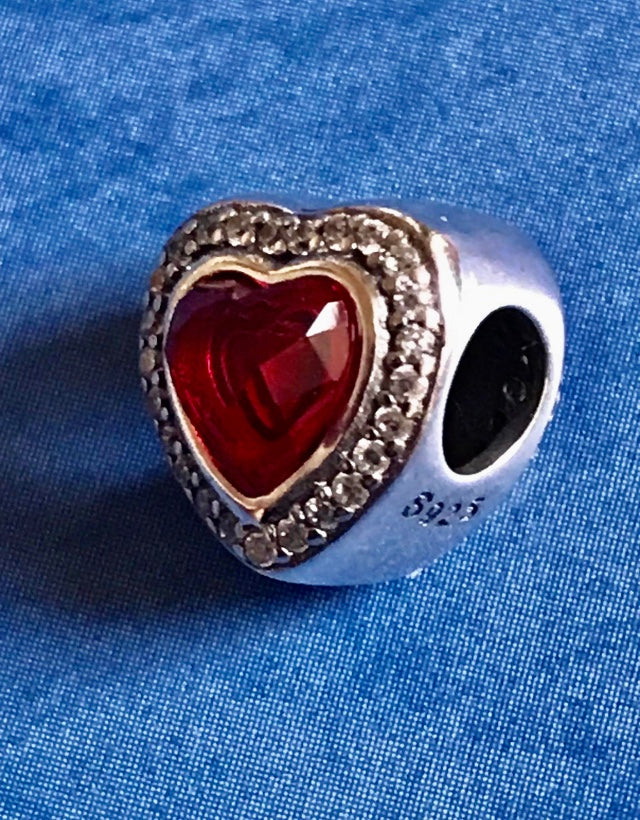 Heart-shaped charm with red center and silver border on a blue fabric background