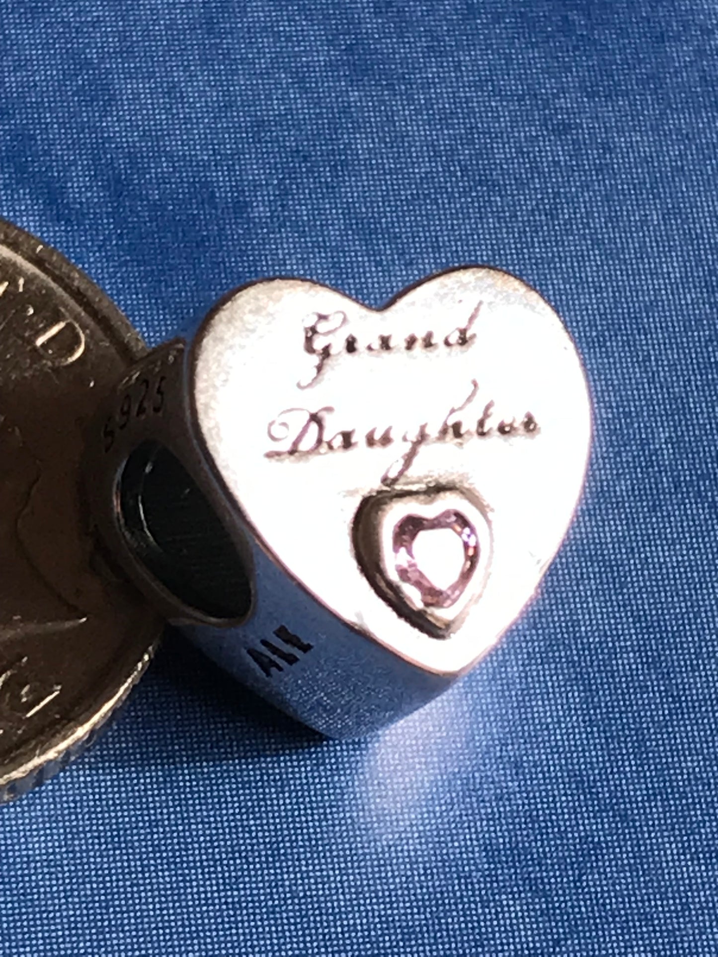 Heart-shaped silver charm with engraved text on a blue fabric background