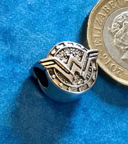 Silver Wonder Woman charm next to a British coin on a blue background
