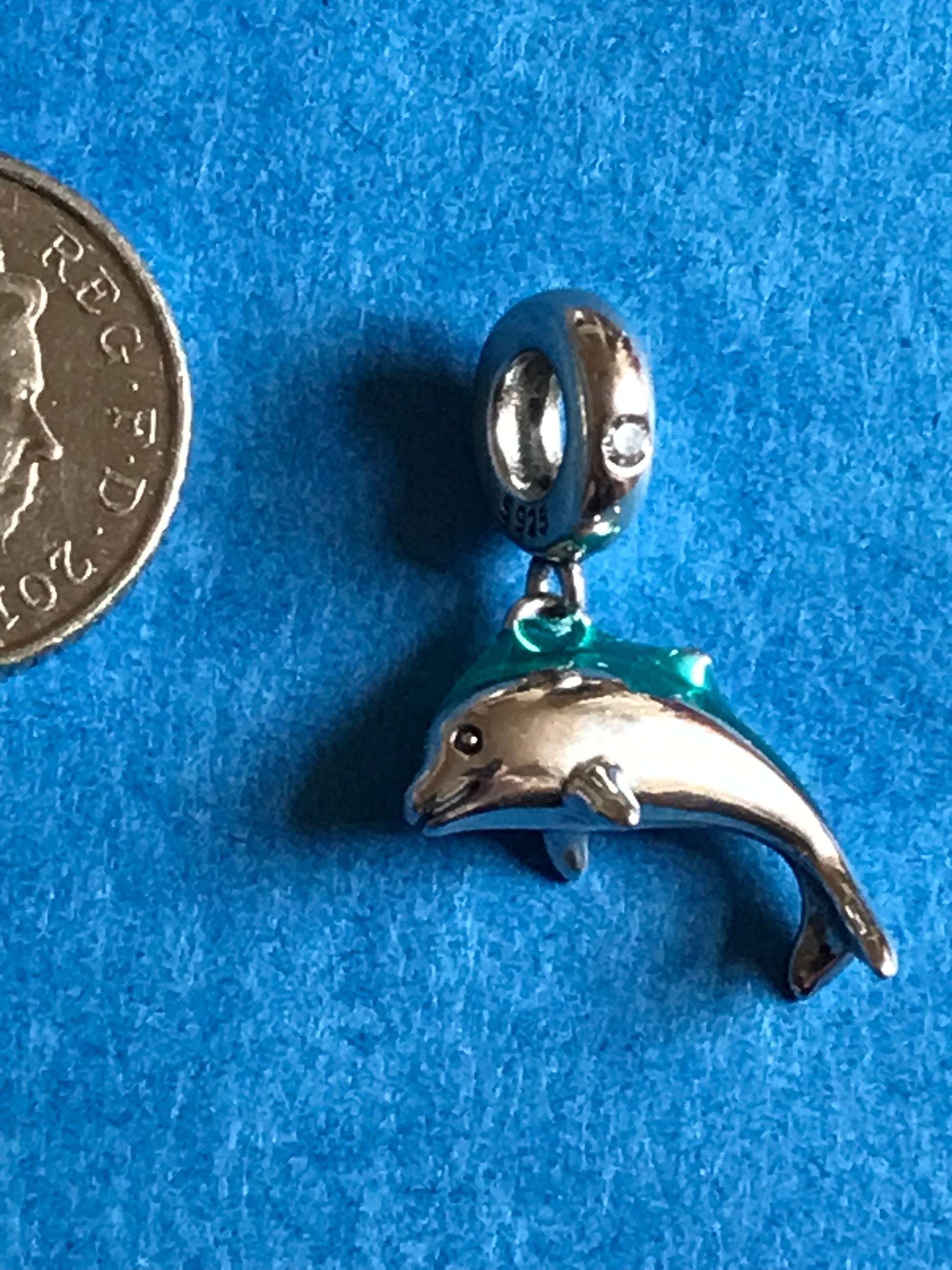 Silver dolphin charm on a blue background with a coin for scale