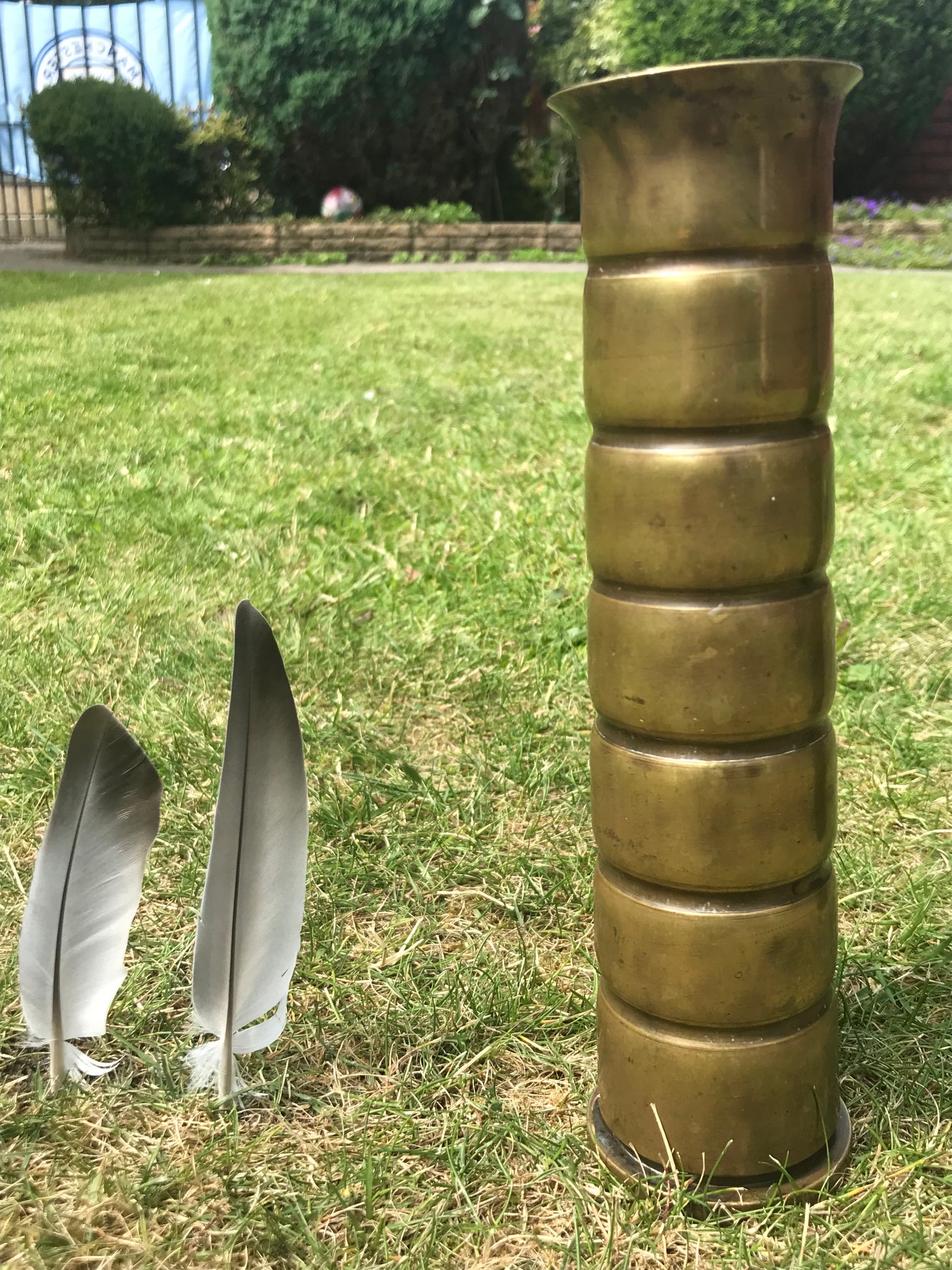 Brass World War Two Trench Art Vase on grass next to two feathers for scale