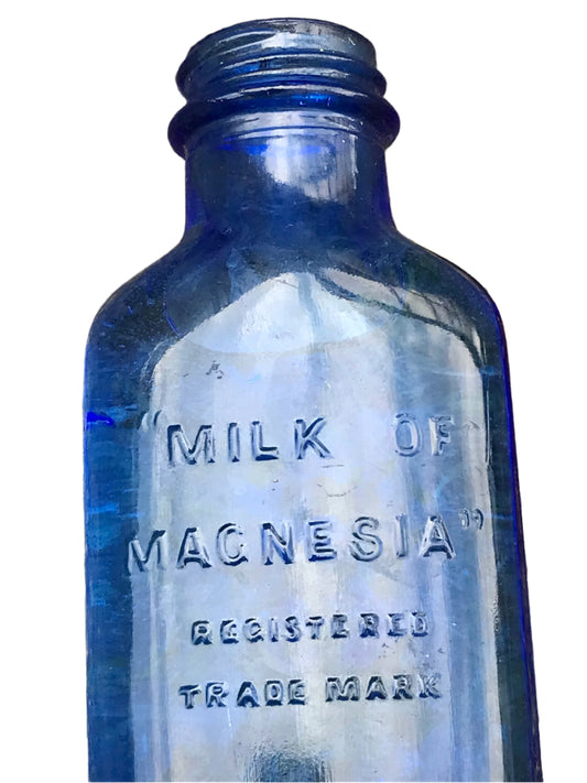 Vintage blue glass bottle labeled 'Milk of Magnesia' on a white background