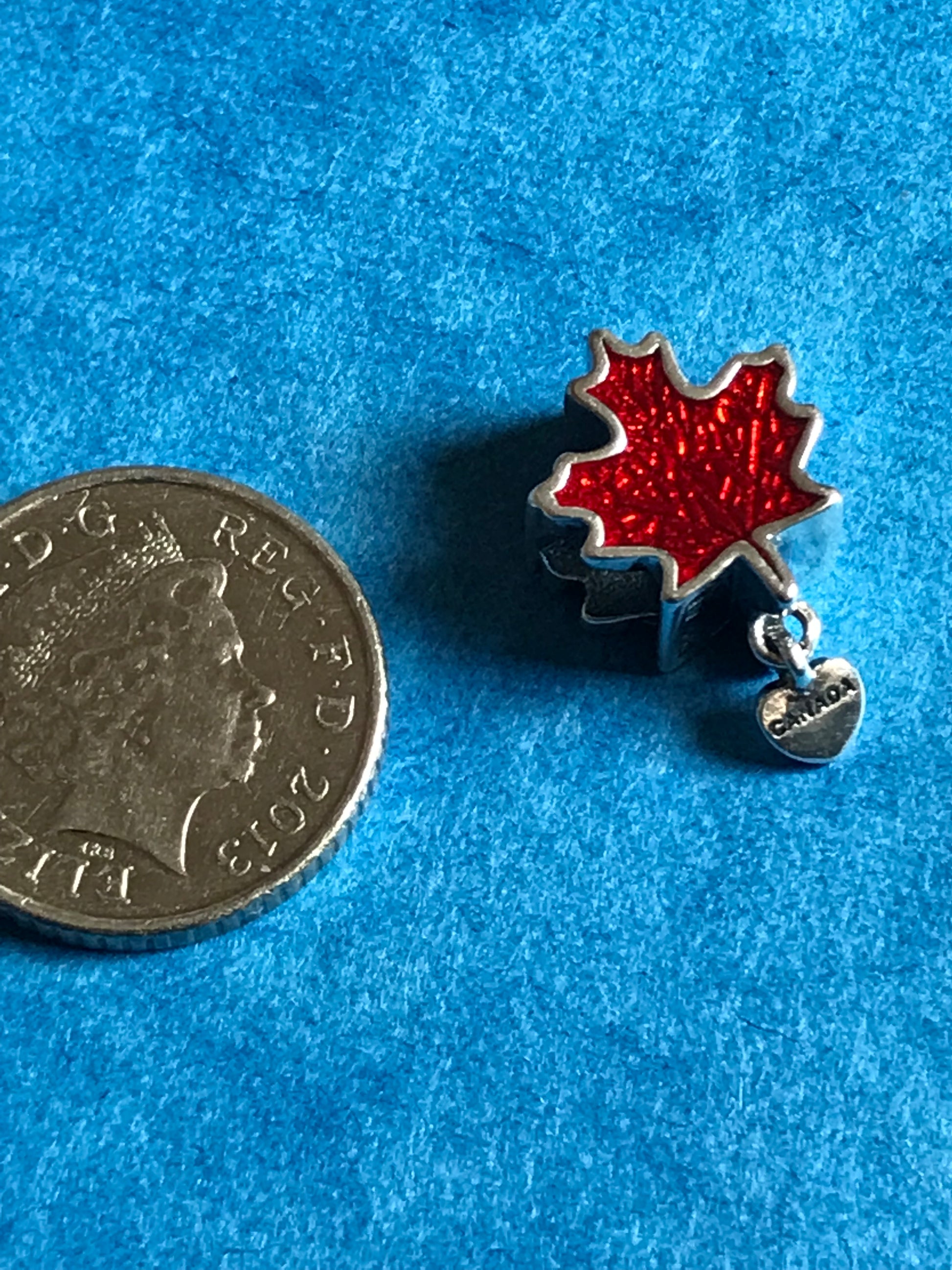 Red maple leaf charm on a blue background with a coin for scale