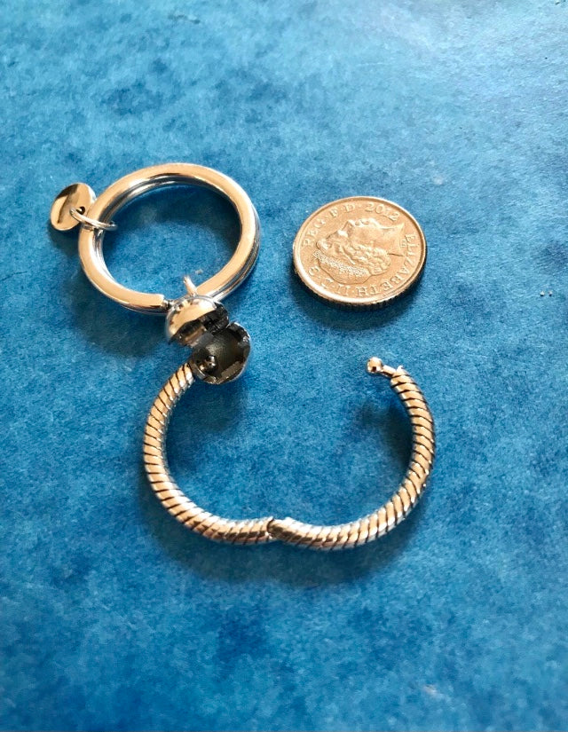 Gold and silver keychain for charms next to a coin on a blue textured background