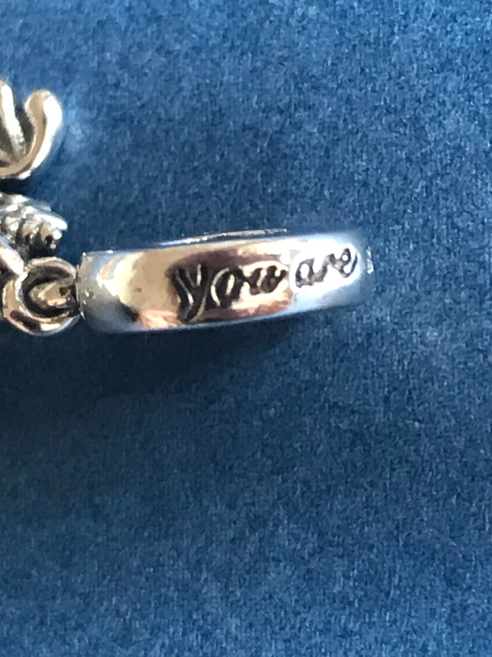 Silver charm with engraved text on a blue background