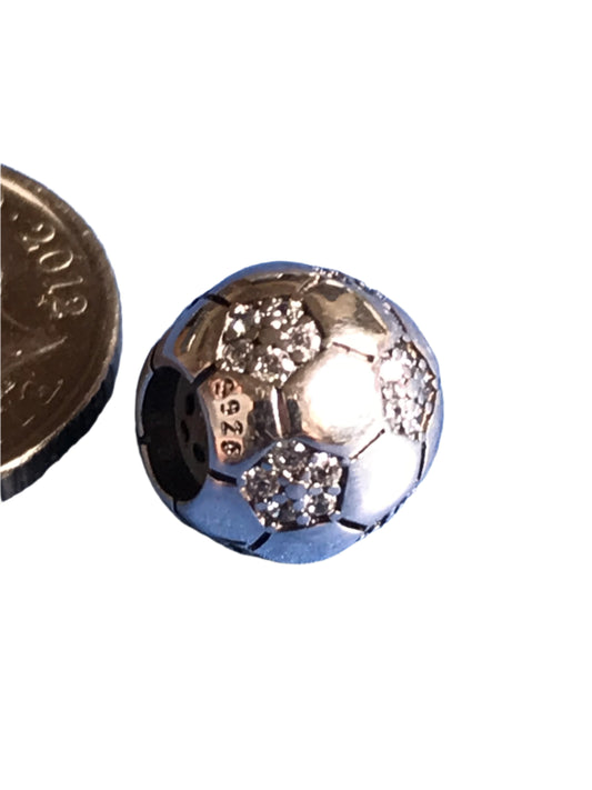 Silver football charm with embedded stones next to a coin for scale on a white background