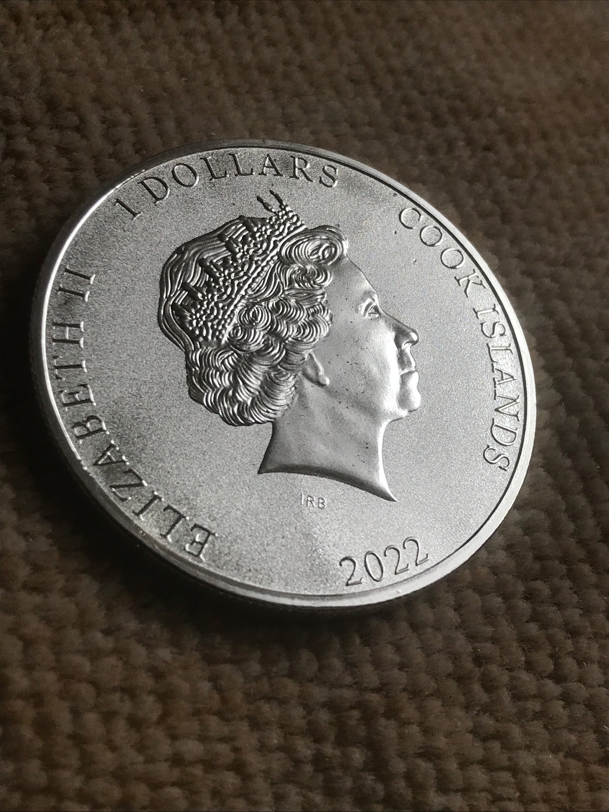 Silver coin with a portrait and text on a textured brown background