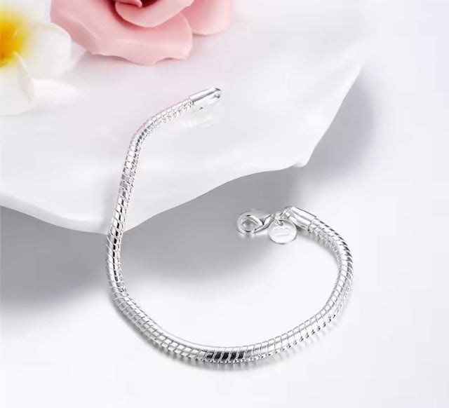 Silver bracelet on a white surface with a pink flower in the background