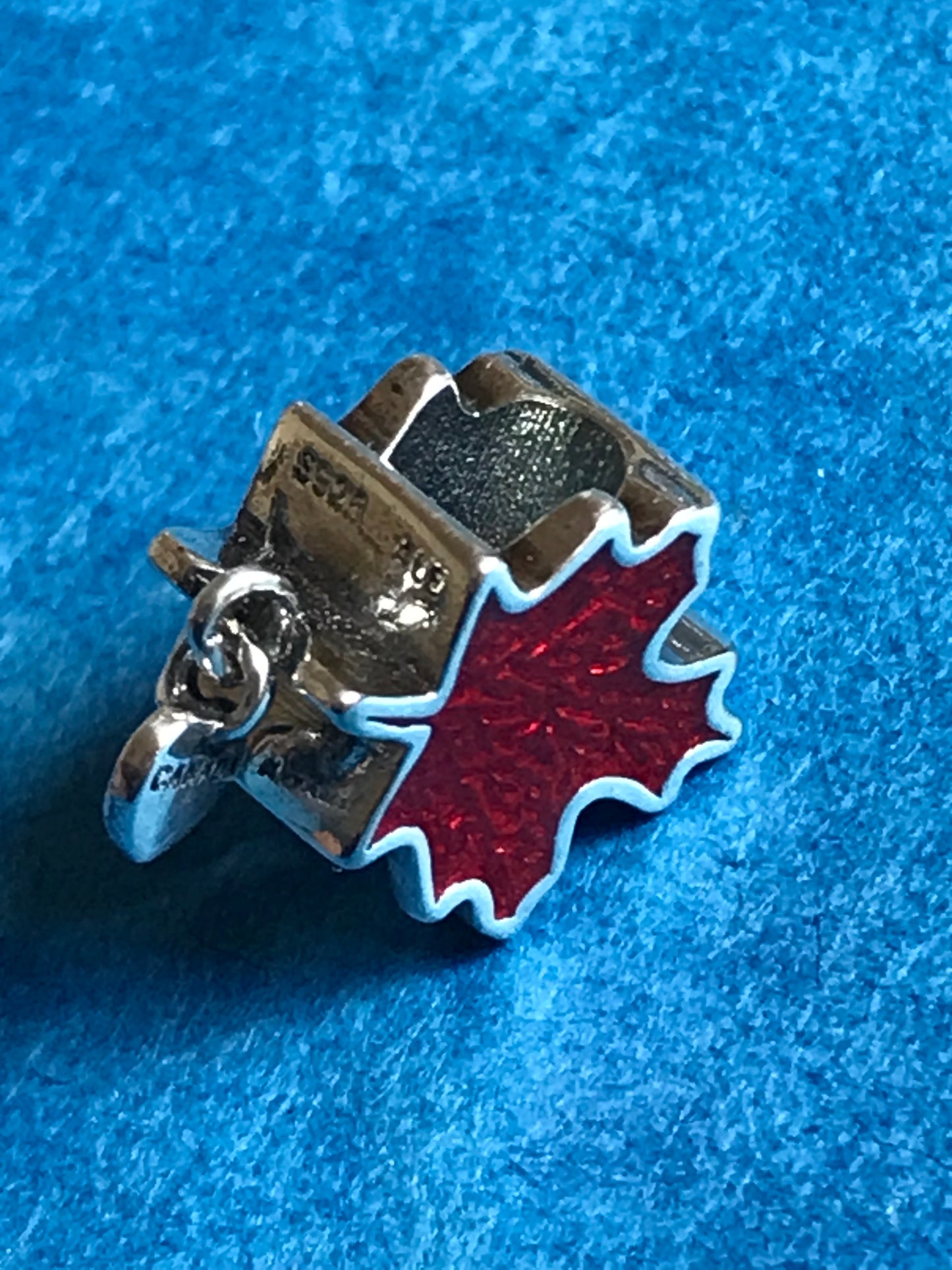 Silver charm with a red maple leaf on a blue textured background