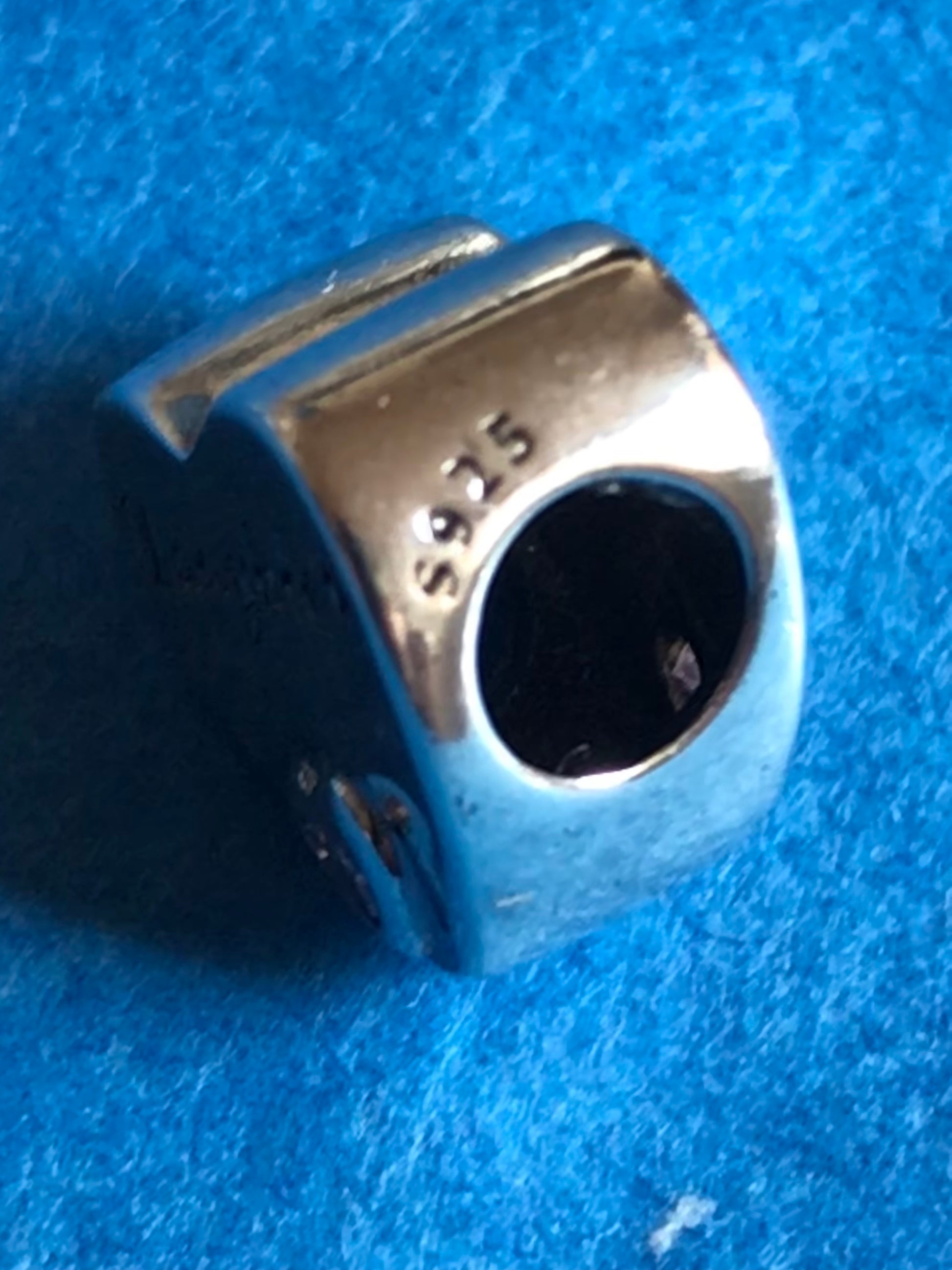 Silver charm with '925' stamp on a blue fabric background