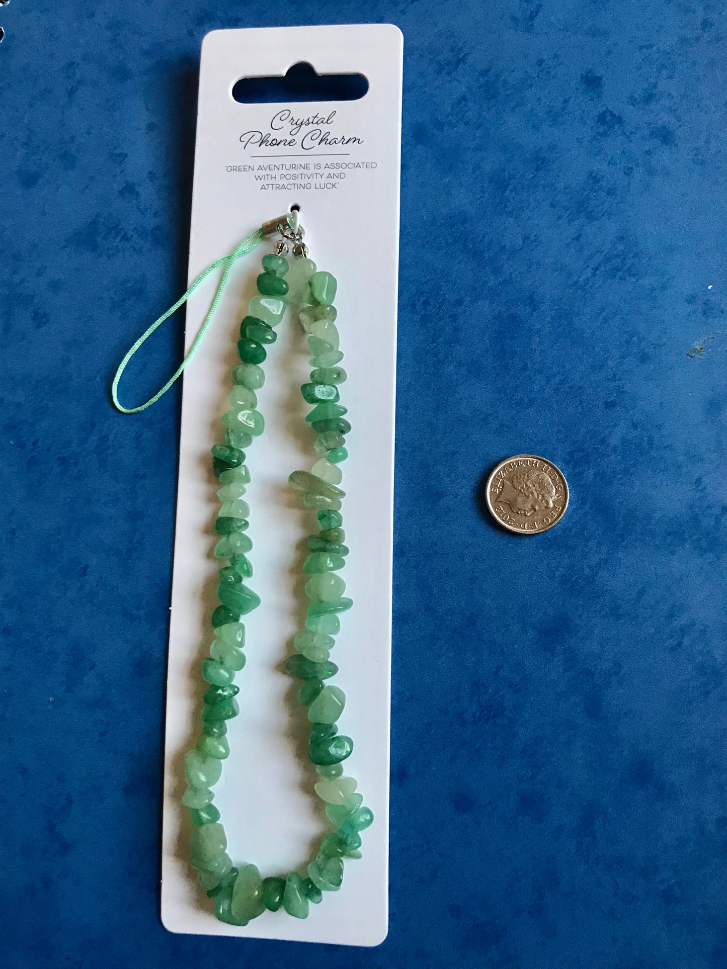Green crystal phone charm on a white card with a coin for scale, against a blue background