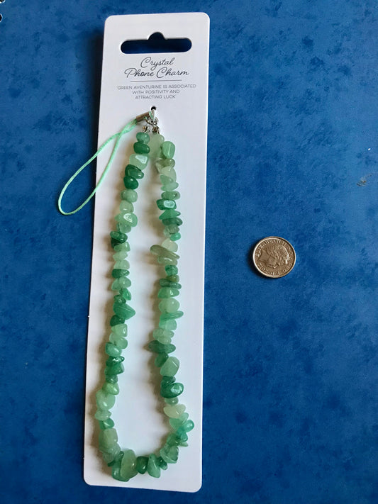 Green crystal phone charm on a white card with a coin for scale, against a blue background