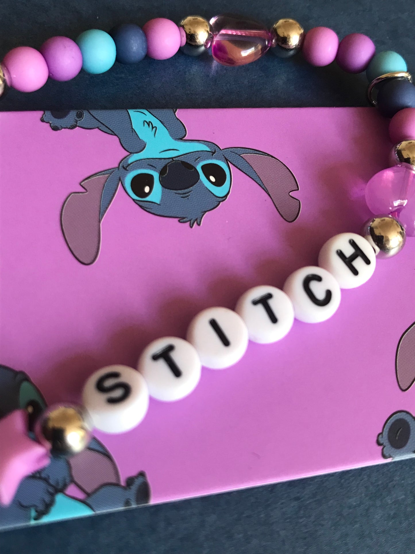 Genuine Hand crafted crystal phone charms spelling 'STITCH' on a pink card with cartoon character