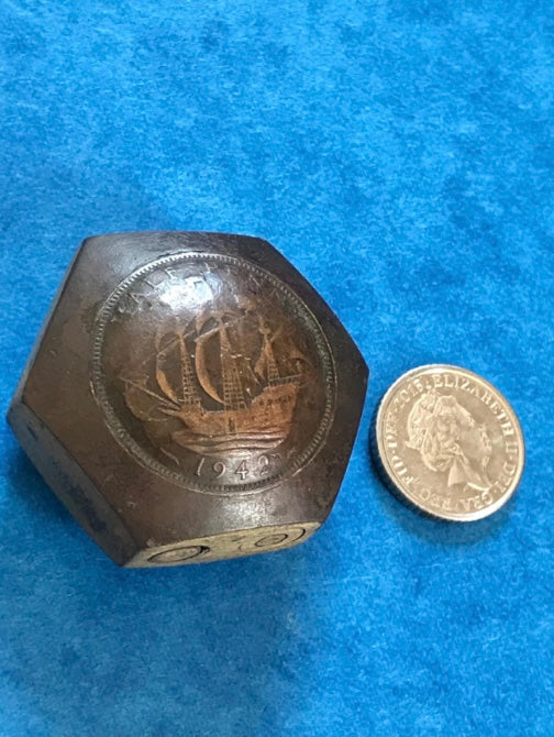 Hexagonal Vintage Genuine WW2 Trench Art 1942 brass lighter with engraved design next to a coin on a blue surface