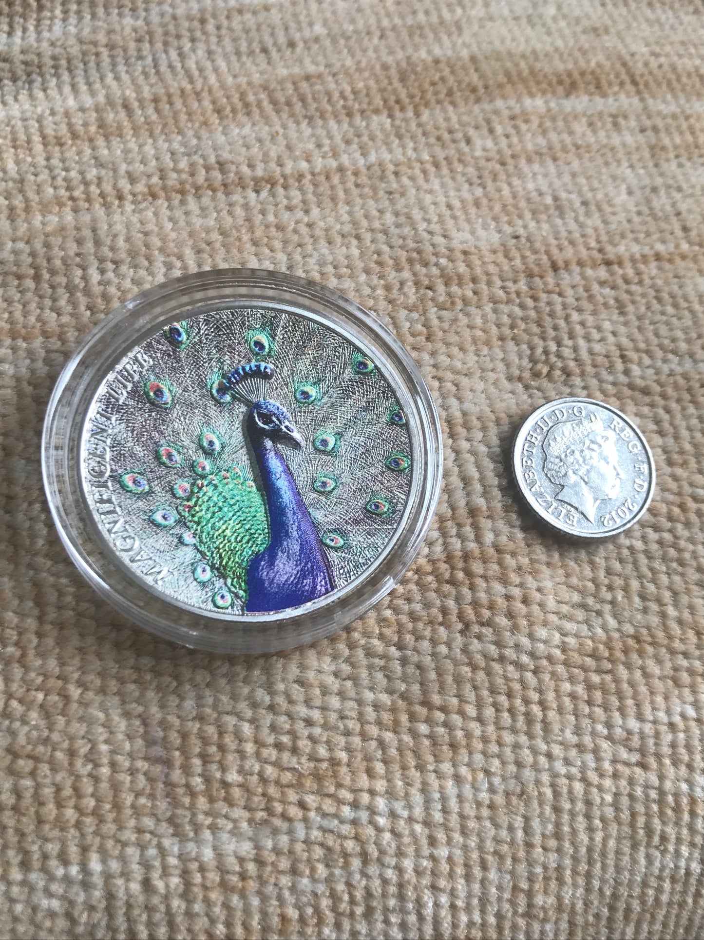 Silver coin with peacock design on a textured fabric background