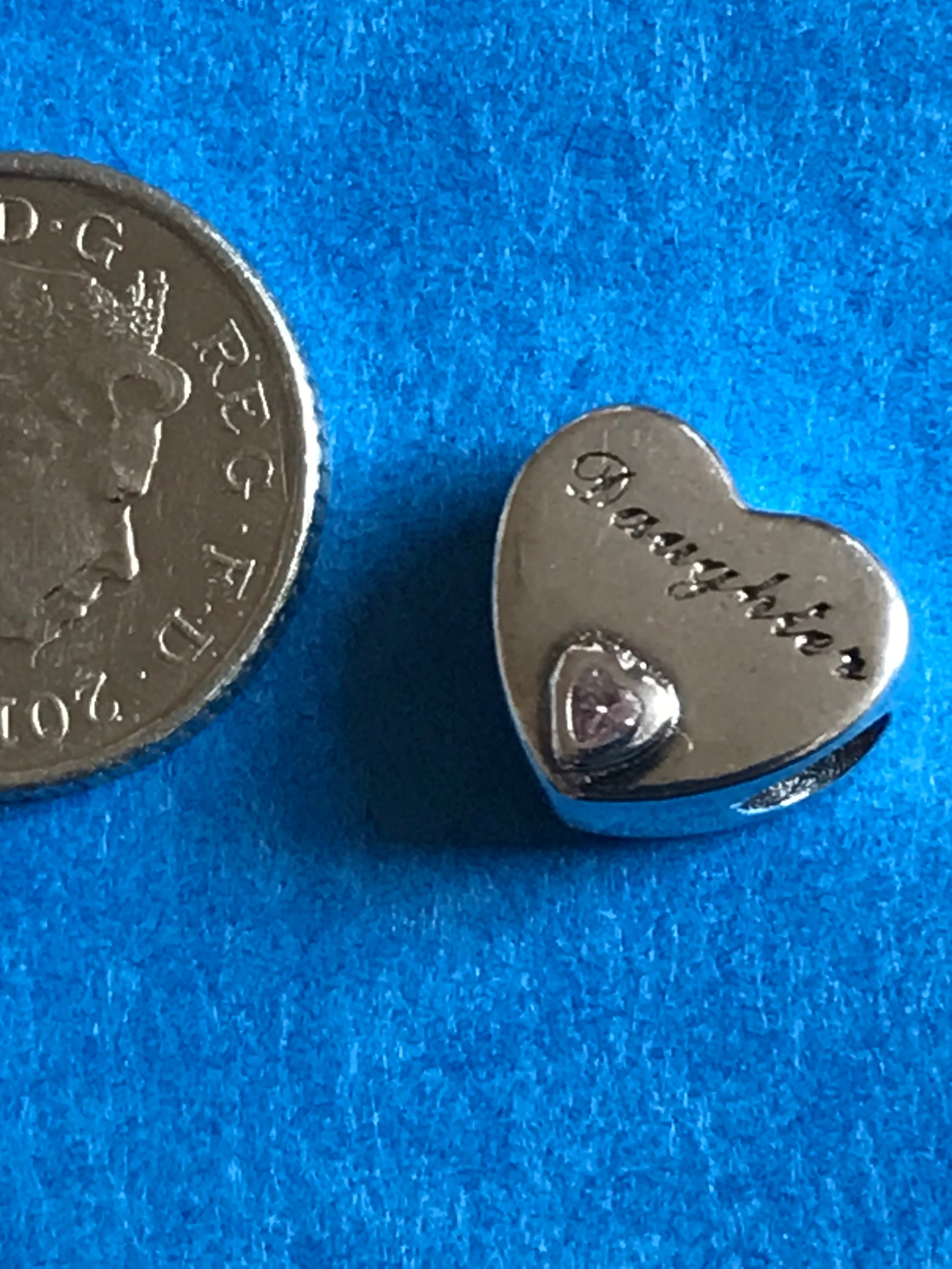 Heart-shaped silver charm with 'Daughter' engraving on a blue background