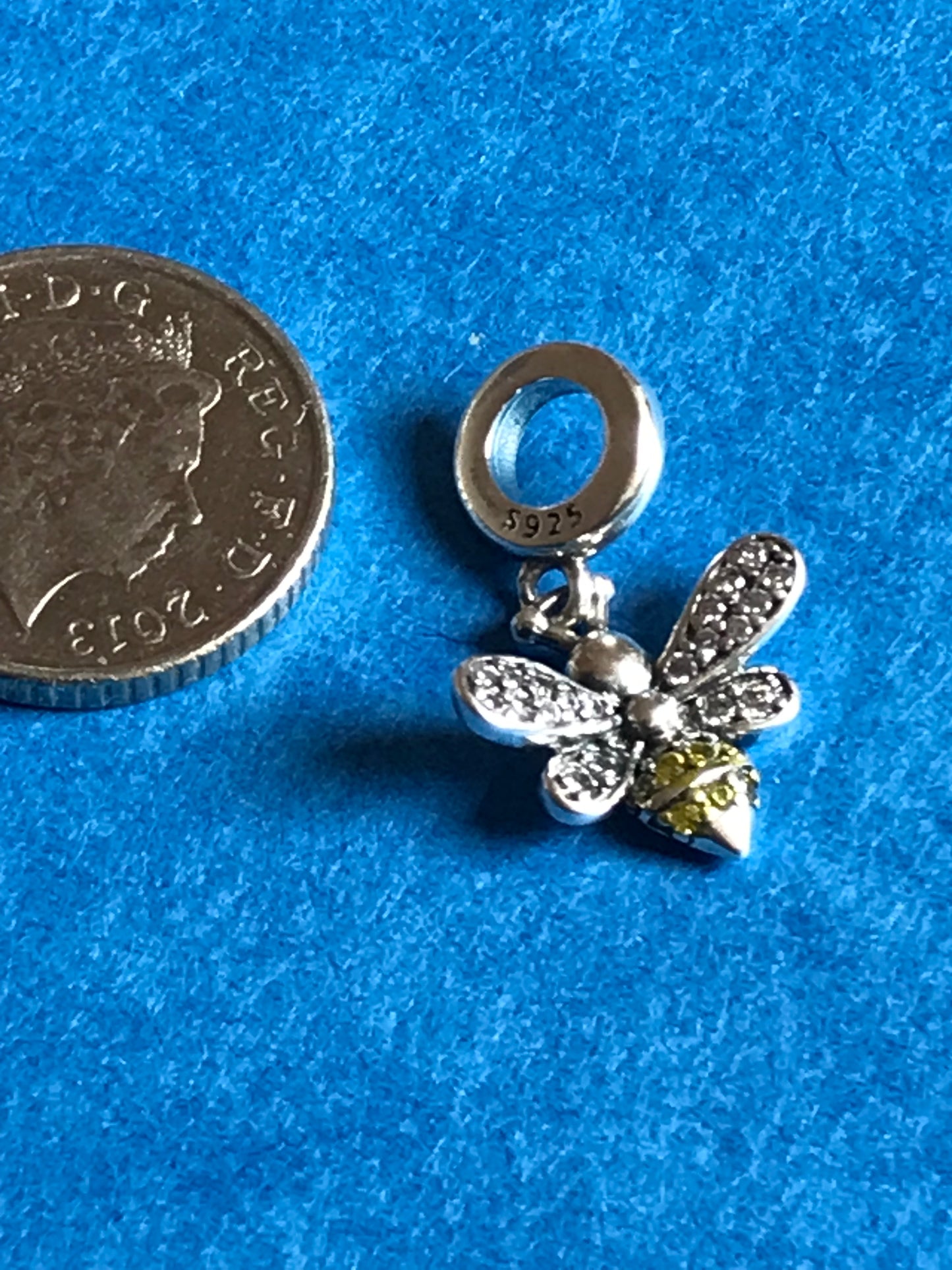 Silver bee charm with yellow gemstone on a blue background, next to a coin for scale charm bracelet 
