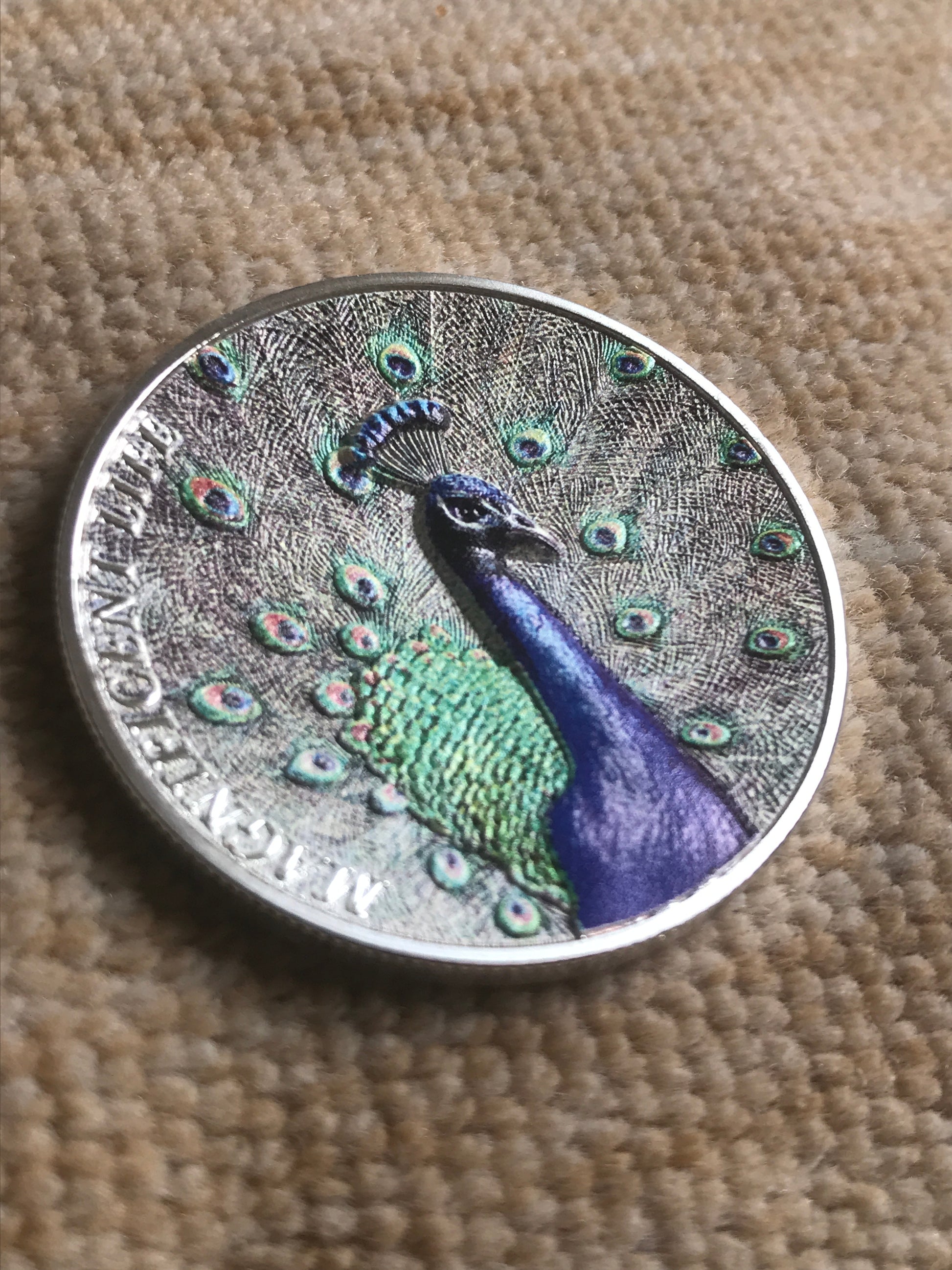 Silver coin with a peacock design on a textured surface