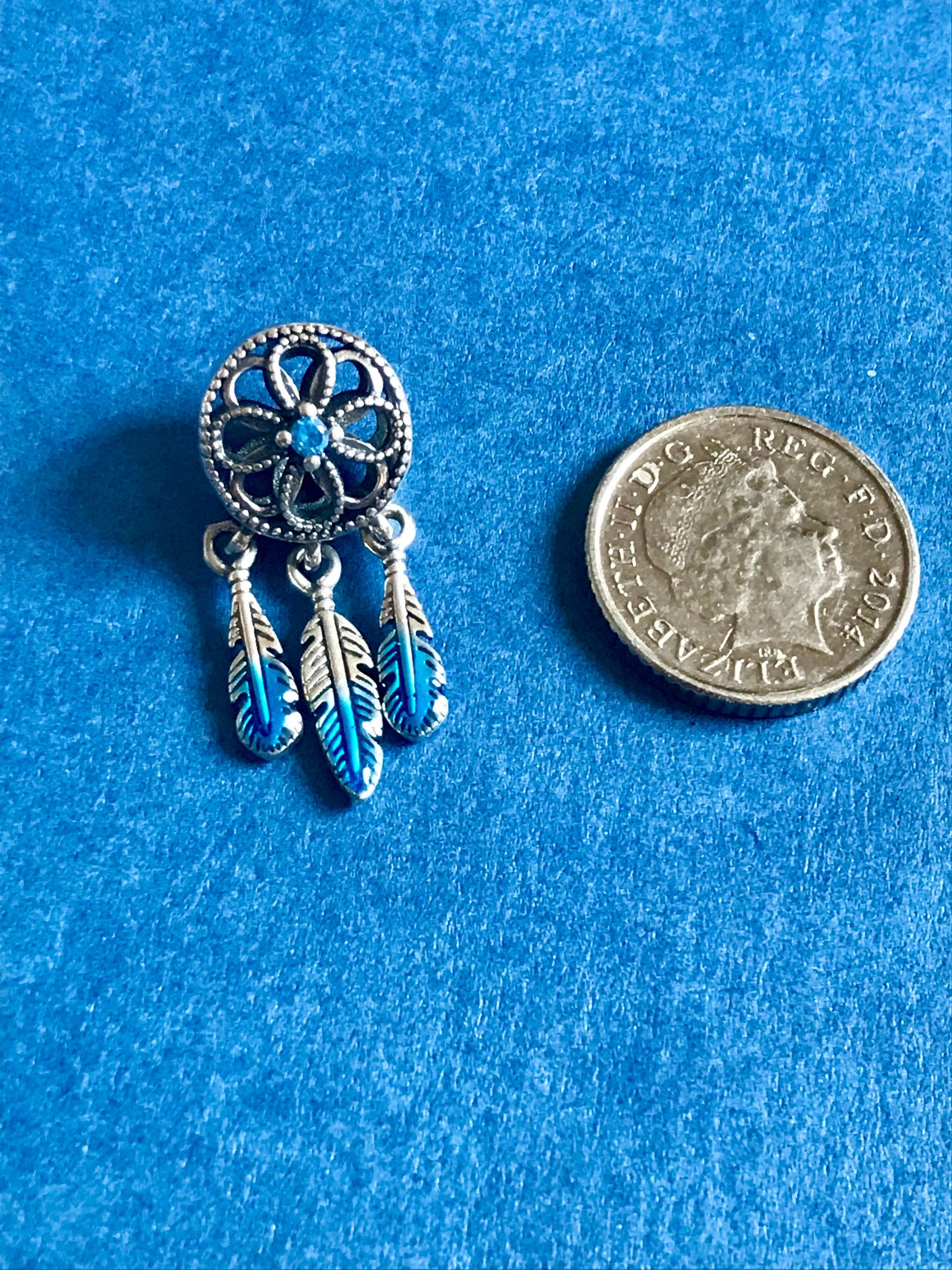 Silver and blue dreamcatcher charm next to a coin on a blue background