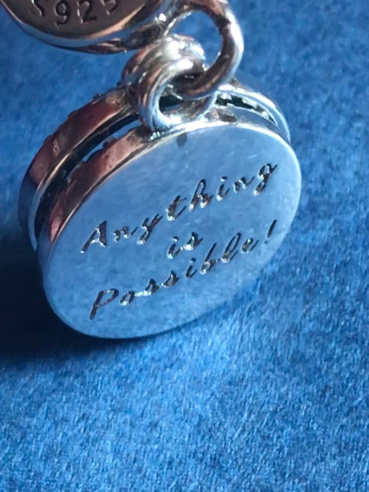 Silver charm with 'Anything is Possible!' engraving on a blue background